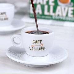 Cup of coffee being poured into a 'Cafe La Llave' cup with a visible brand logo in the background.