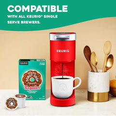 Red Keurig coffee maker with a white mug, Donut Shop coffee box, and K-cups on a beige background.