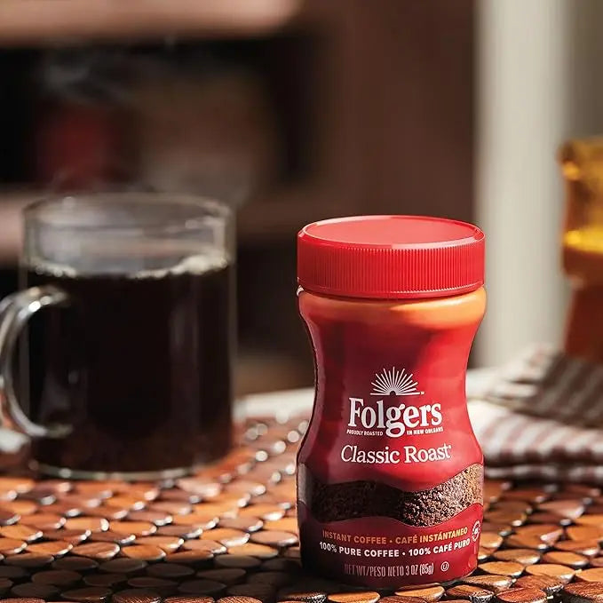 Folgers Classic Roast instant coffee jar on a table with a cup of coffee in the background