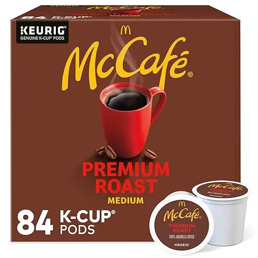 Box of McCafé Premium Roast K-Cup pods with a red cup and coffee beans on a brown background.